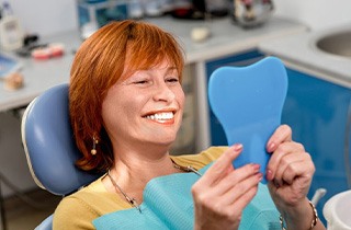 Woman in patient’s chair smiling in the mirror