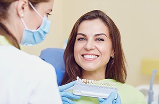 Woman smiling as dentist holds shade guide to her teeth