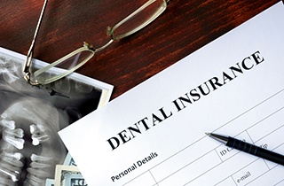 Top of dental insurance form with x-ray, glasses, money, and pen