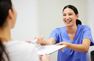 Woman in blue scrubs handing application on clipboard to patient
