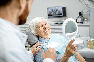 An elderly woman admiring her restored smile in a hand mirror