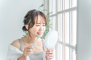 a woman brushing her teeth and examining her smile