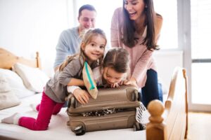 Man, woman, and two little girls laughing while closing a brown suitcase together