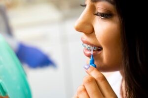 Profile view of a woman with brown hair and periwinkle nails brushing her braces