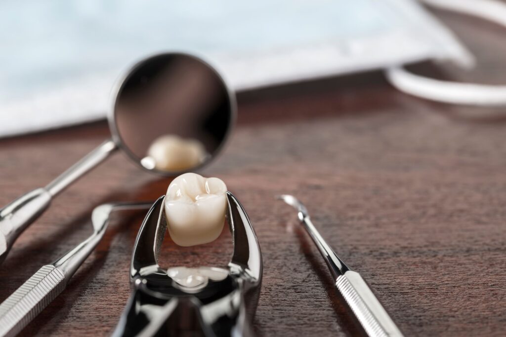 Extracted tooth held by forceps next to dental instruments on wooden surface